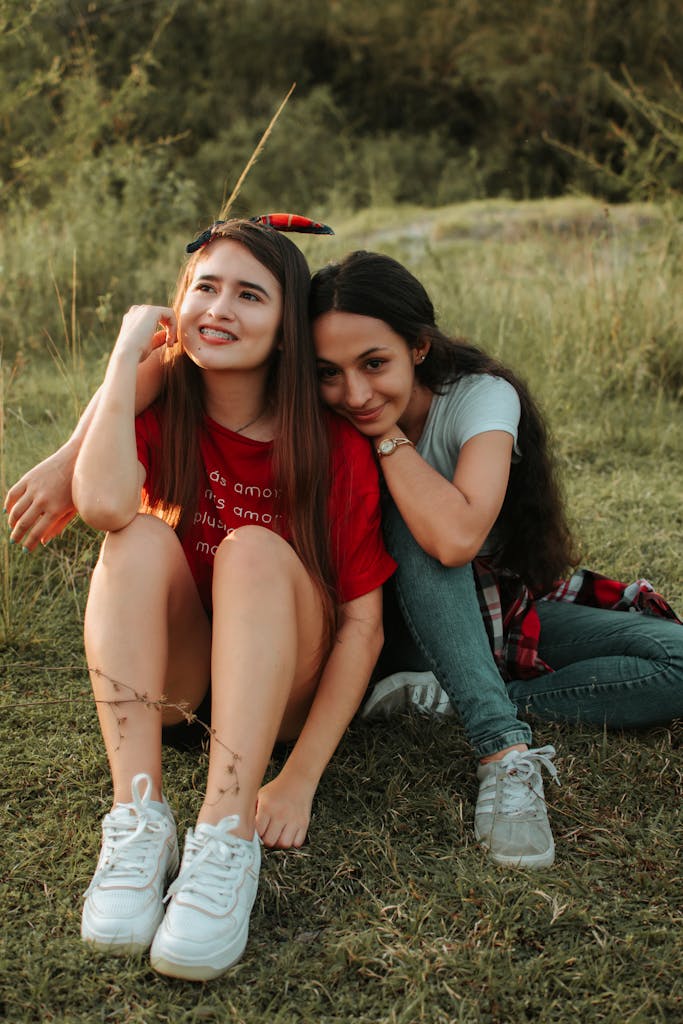 Two smiling teenage girls sitting together outdoors enjoying a sunny day.