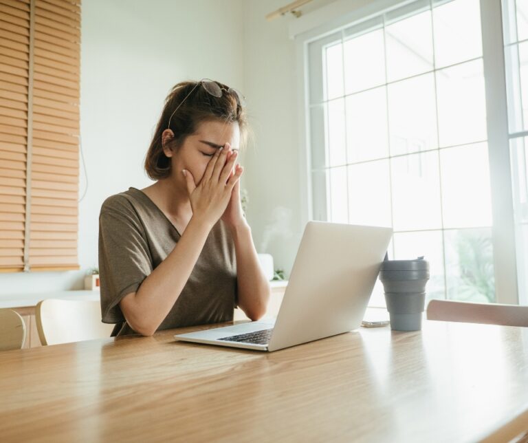 Tired woman working on a laptop while looking overwhelmed and exhausted