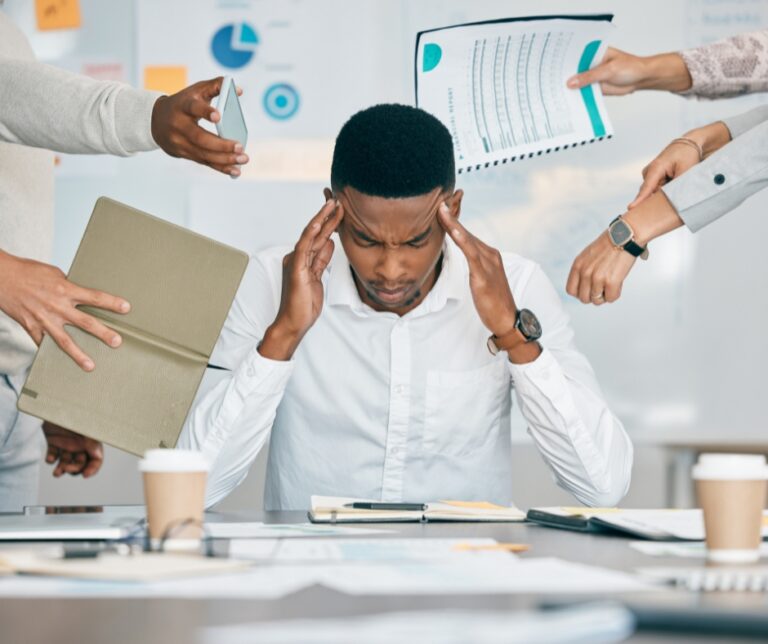 Overwhelmed man sitting at his desk surrounded by work, responsibilities, and distractions